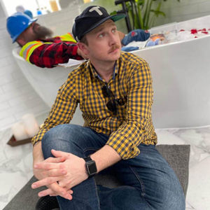 Director Joe Harris gazes wistfully into the distance while sitting in front of a bathtub with a construction worker soaking in it